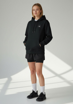 Layer Run Club black hoodie front view worn by female runner standing relaxed