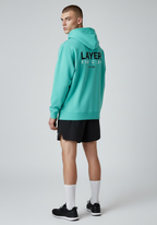 Male athlete wearing the Layer Run Club hoodie in green, back view showing large Layer Run Club print, styled with running shorts.