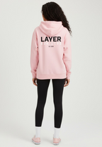 Female athlete wearing the pink Layer Run Club hoodie, back view with bold Layer Run Club branding.