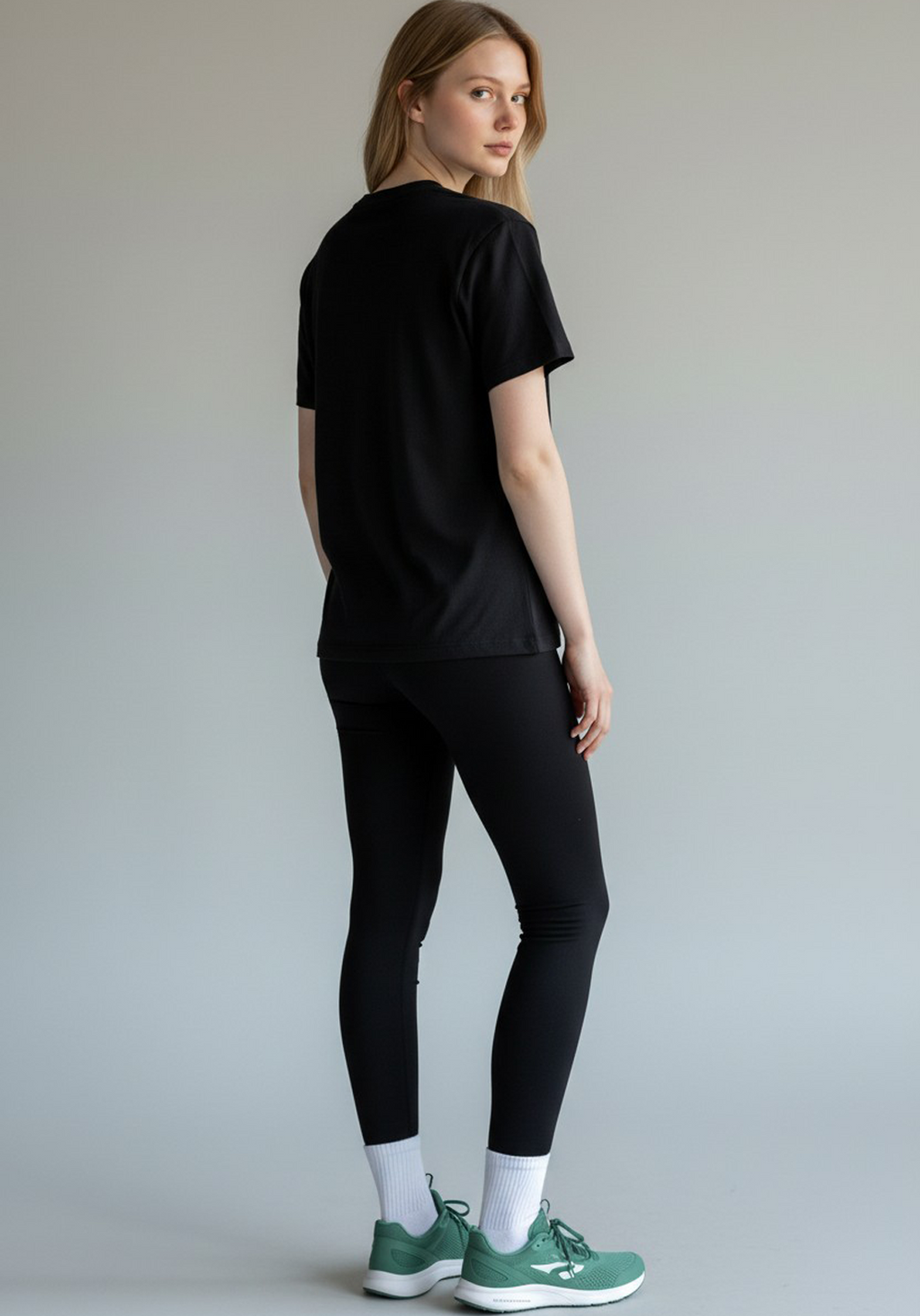 Rear view of a woman wearing a black Layer Performance Sport Signature Tee and black leggings, looking over her shoulder.