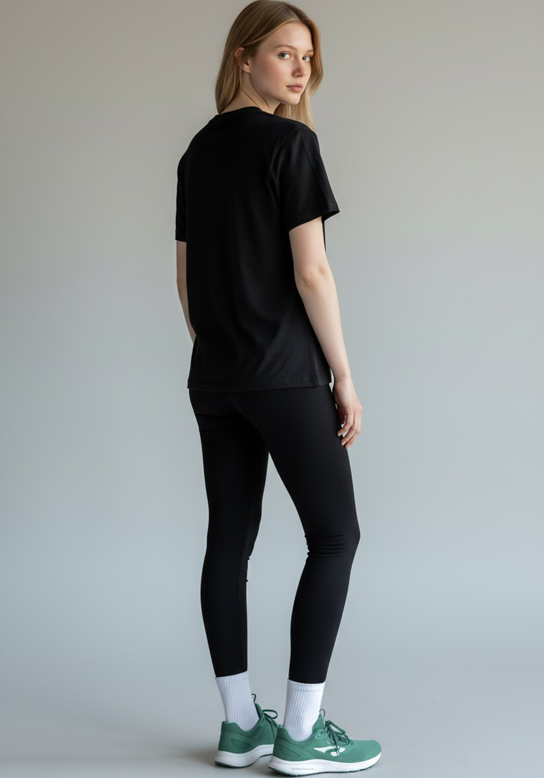 Rear view of a woman wearing a black Layer Performance Sport Signature Tee and black leggings, looking over her shoulder.