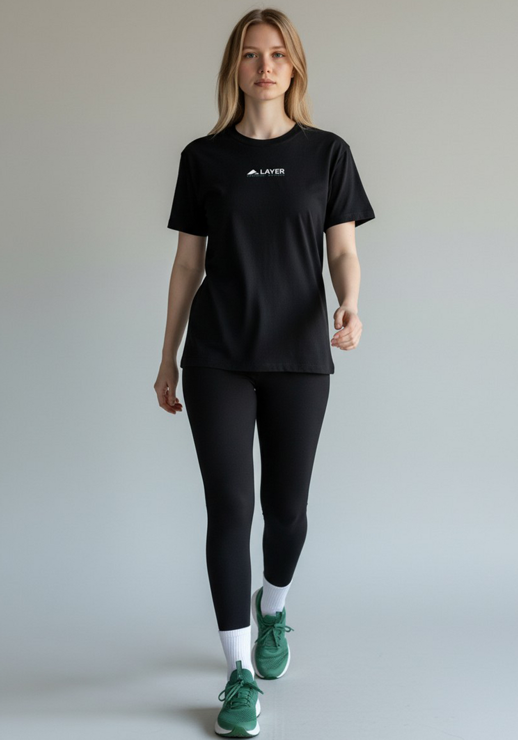 Woman walking forward wearing a black Layer Performance Sport Signature Tee, black leggings, and white socks.