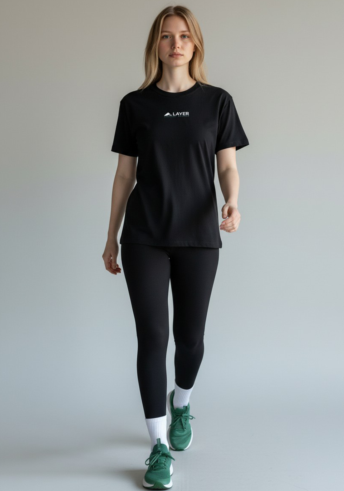 Woman walking forward wearing a black Layer Performance Sport Signature Tee, black leggings, and white socks.