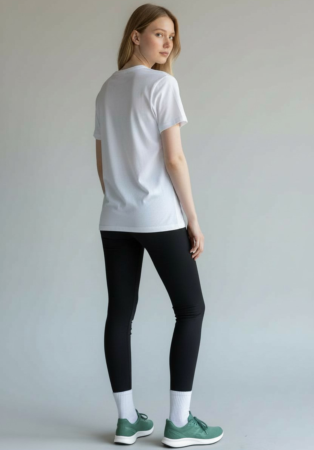 Rear view of a woman wearing a white Layer Performance Sport Signature Tee and black leggings, looking over her shoulder.