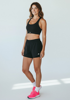 Layer Women’s Performance Bra in black – full-body on-model view paired with running shorts and bright trainers