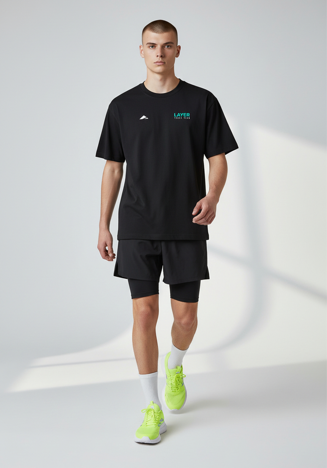 Model walking in the black Layer Track Club Tee styled with training shorts for casual wear.