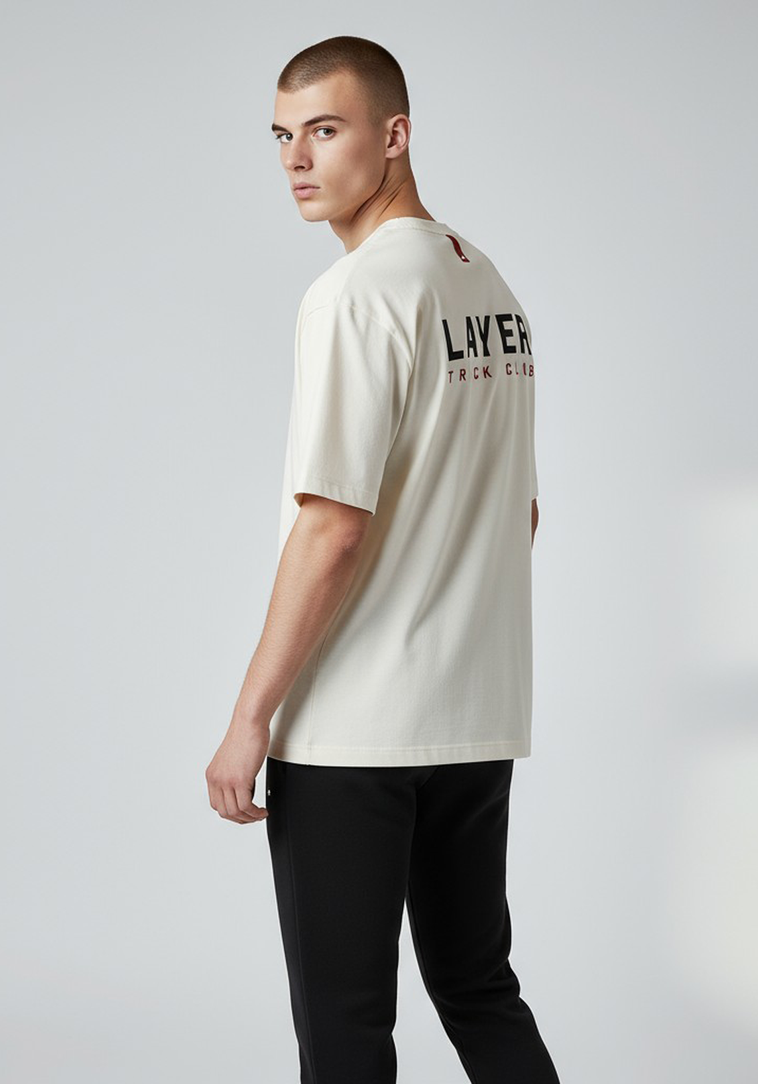 Layer Track Club Tee in Dune White – angled back view on model showing bold LAYER TRACK CLUB print and relaxed fit