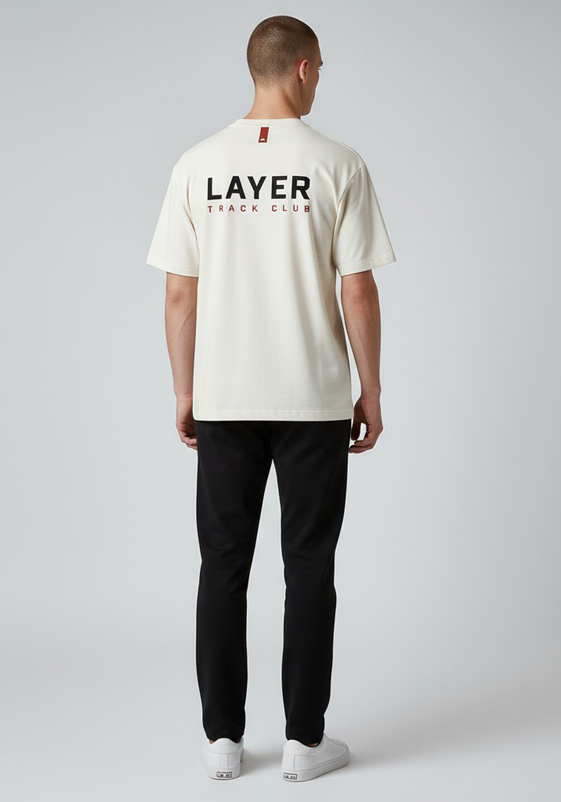 Layer Track Club Tee in Dune White – back view on model highlighting large graphic print and red detail tab