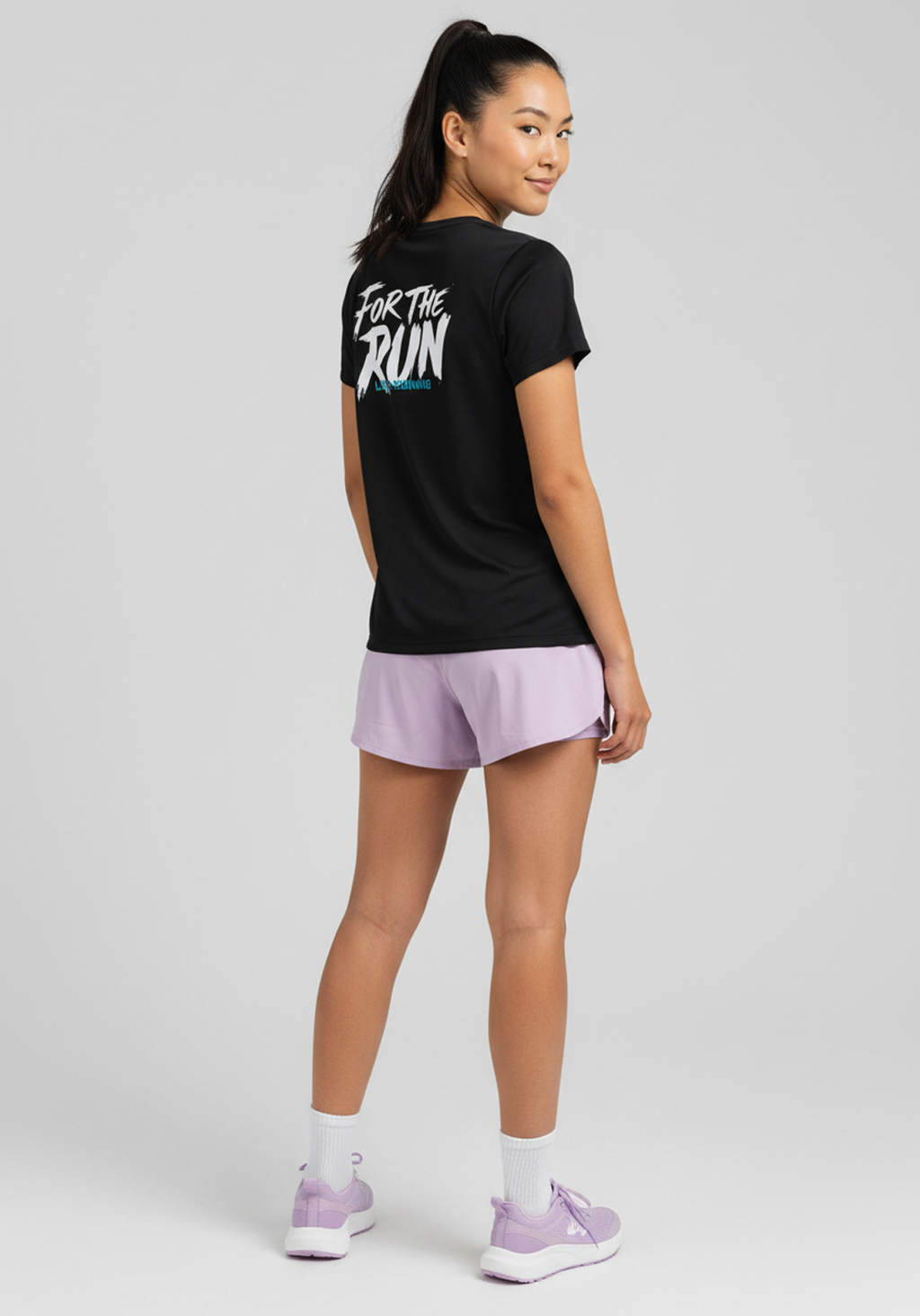 Three-quarter rear view of woman wearing black Layer FTR Graphic Running Tee during run-ready pose.